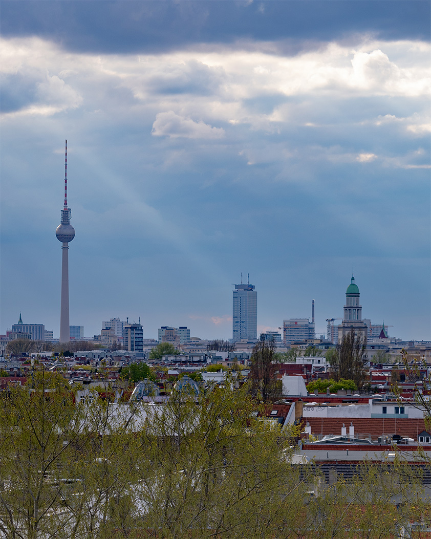 Blick über die Dächer Berlins mit Fernsehturm und den Türmen des Frankfurter Tors unter einem dramatischen Wolkenhimmel